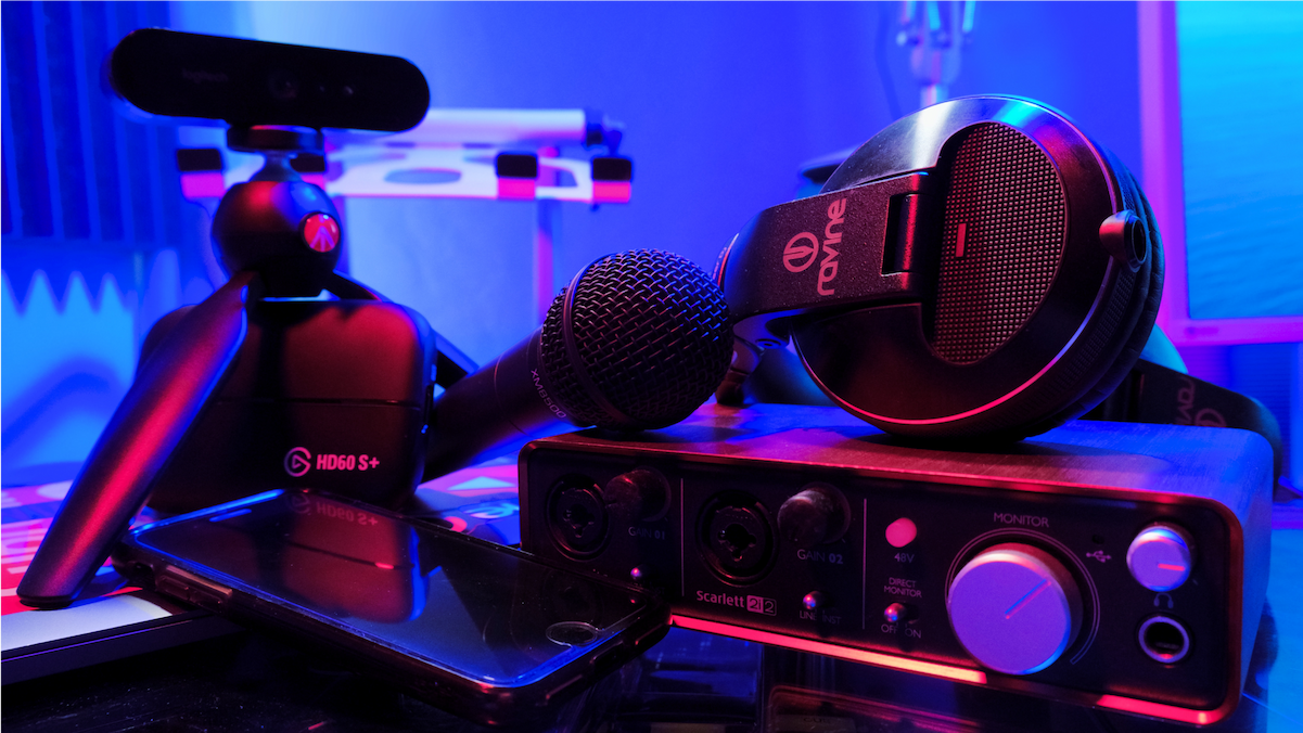 A close-up of content creation material: a microphone, headphones, a webcam, an audio interface, and a phone.